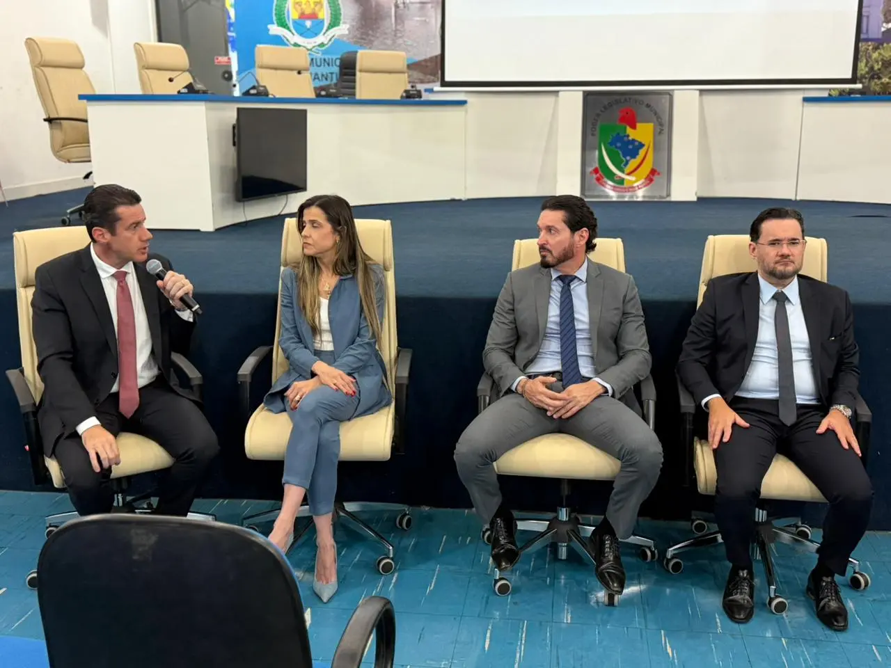 A imagem mostra quatro magistrados — três homens de terno e uma mulher de conjunto azul — sentados em cadeiras executivas bege sobre o palco do plenário. O homem na ponta esquerda fala ao microfone, enquanto os demais o escutam com atenção.