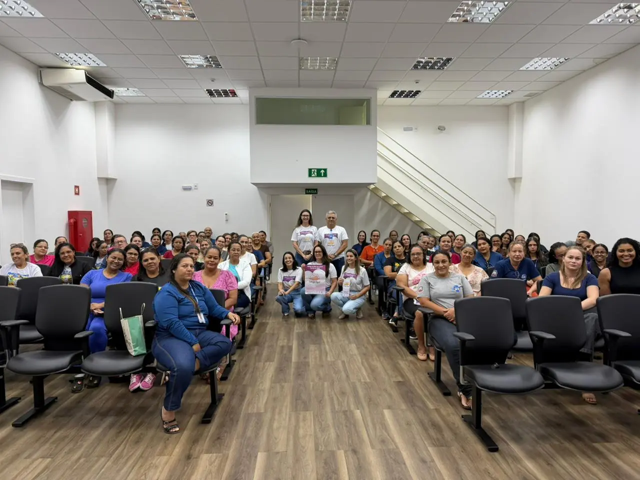 Participantes da capacitação sobre entrega voluntária realizada no Fórum de Tangará da Serra posam para foto no plenário da unidade. Os profissionais estão voltados para a câmera. Ao centro, a juíza Raiza Vitória de Castro e integrantes da equipe seguram materiais de divulgação da campanha.
